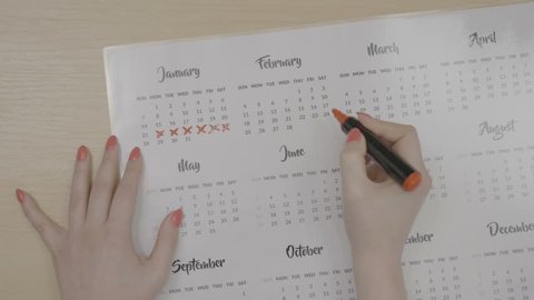 Top view of a young female hands with red nails marking dates on calendar planning birth control