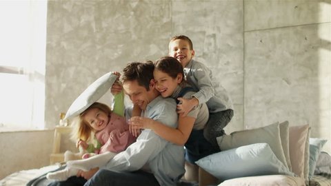 A young father and three children embrace sitting on the bed. Happy fatherhood. Father's Day.