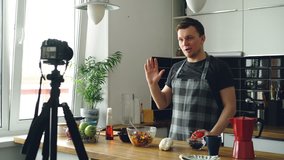 Handsome guy recording video food vlog about healthy cooking on digital camera in the kitchen at home. Vlogging and social media concept
