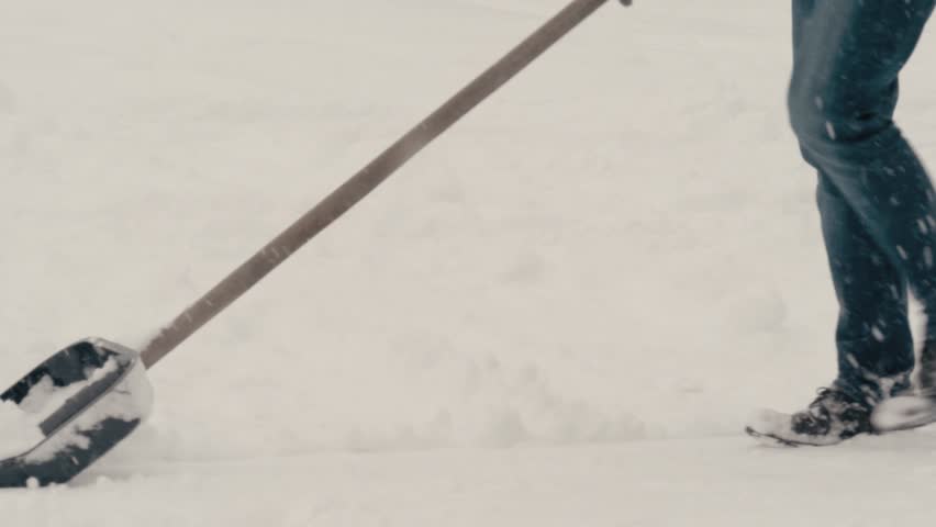 A young man clears snow with a shovel.