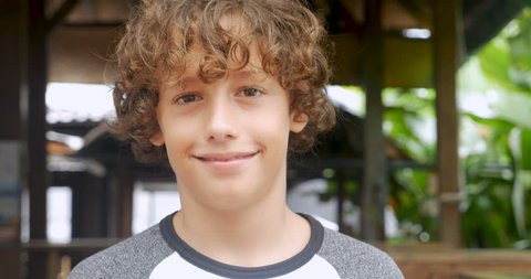 Portrait of a cute young 11 - 12 year old boy with curly hair smiling and looking at the camera