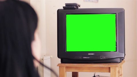 Woman Watching an Old 90s TV with Green Screen at Home. Back View. You can replace green screen with the footage or picture you want with “Keying” effect in AE  (check out tutorials on YouTube). 