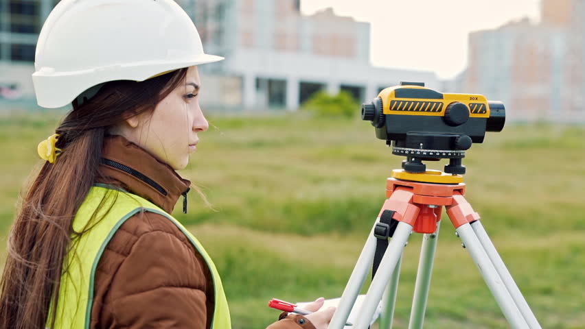 young woman surveyor in green work clothes and helmet adjusts the equipment, produces calculations and writes to the notebook on the construction site. The concept of landscape design, geodesy Royalty-Free Stock Footage #1008492196