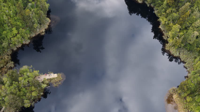 A birds eye view drone shot flying over the clear reflective surface of Lake Matheson.
