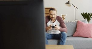 Young handsome man sitting on the couch in the living room and playing video games. Inside