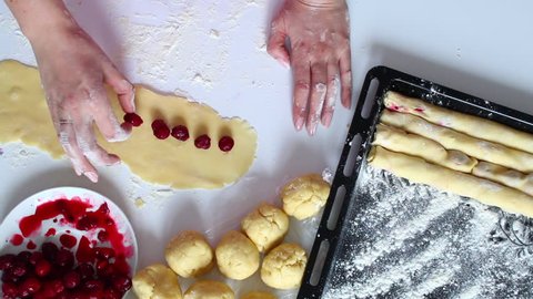 The process of making a cake. The woman wraps the filling in the dough. Next in a plate is a filling frozen berries of cherries and raspberries.