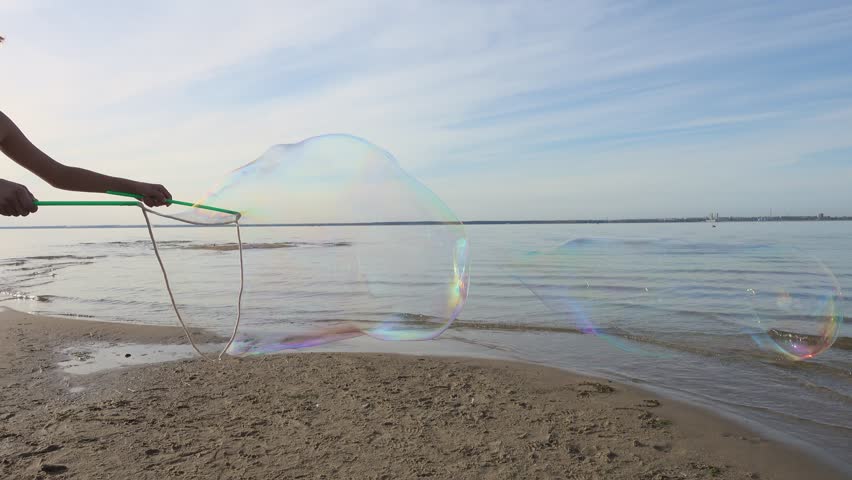 Boy making big soap bubbles on the beach at a sunset. Summer holidays at sea.