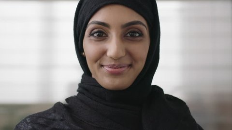 close up portrait of professional young muslim business woman looking at camera smiling happy wearing traditional headscarf in office background