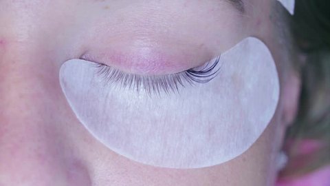 Extreme close up woman eye. Eyelash extension procedure. Young woman in a beauty salon. Cosmetologist begins to glue eyelashes