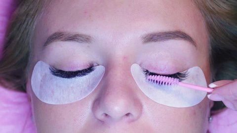 Close up woman face. Eyelash extension procedure. Cosmetologist combing eyelashes with a brush