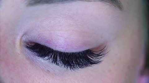Extreme close up woman eye. Eyelash extension procedure. Cosmetologist combing eyelashes with a brush