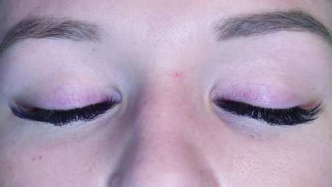 Close up woman eyes. Eyelash extension procedure. Cosmetologist combing eyelashes with tweezers