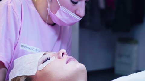 Medium shot. Eyelash extension procedure. Young woman and cosmetologist in a beauty salon