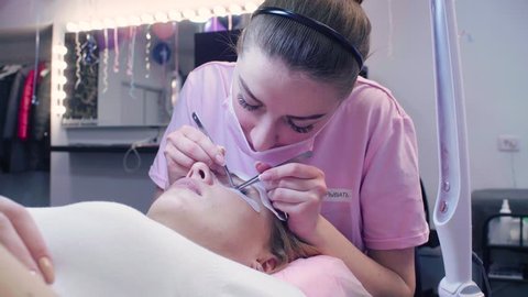 Medium shot. Eyelash extension procedure. Young woman and cosmetologist in a beauty salon