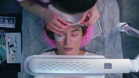 Top view, time lapse, medium shot. Eyelash Extension Procedure. Young woman in a beauty salon