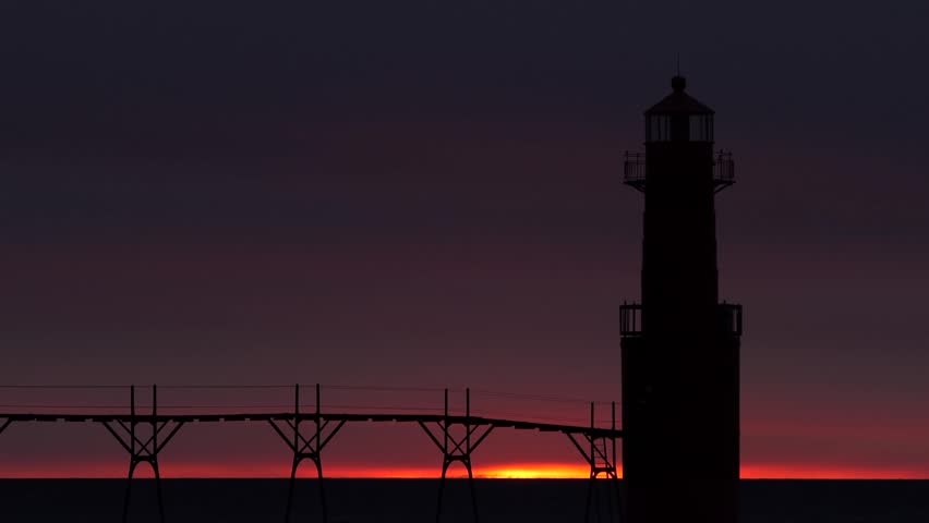 Iconic Lighthouse silhouetted against fiery Lake Michigan twilight, time lapse.
