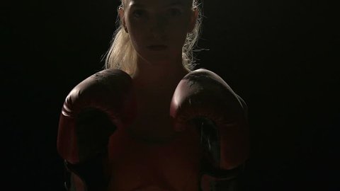 Woman ready to fight. Punches her gloves together to create powder smoke. White young beautiful fit woman. Shot in slow motion. Film look filter.