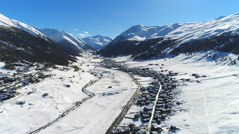 Aerial view of Italian Alps in snowy winter, mountain peaks and ski slopes covered with snow, sunny day with clear blue sky - ski resort Livigno, Lombardy, Italy from above, 4k UHD