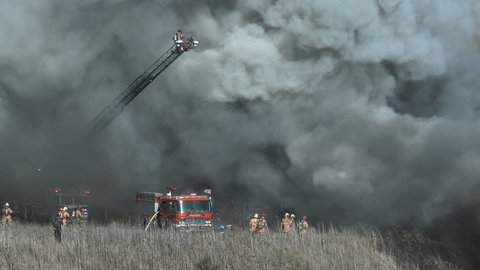 Fire fighters have their work cut out for them as they try to contain a huge fire during high winds causing black smoke.