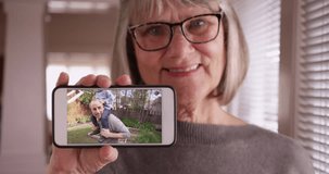 Kind old lady showing smartphone footage of her family playing in backyard. Charming elderly white female holding phone up to camera with video of her family playing. 4k