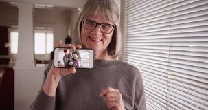 Caucasian grandmother showing video clip of family during Christmas on phone. Elderly woman holding smartphone with video of children and grandkids playing. 4k