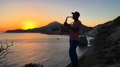 The saxophonist plays in the rays of the sunset on a cliff overlooking the sea