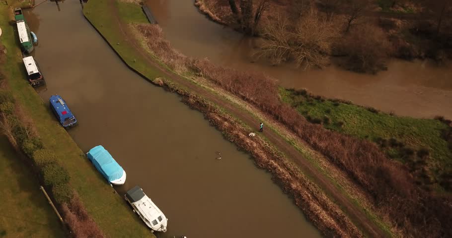 Aerial drone footage of a person walking their dog along a canal.