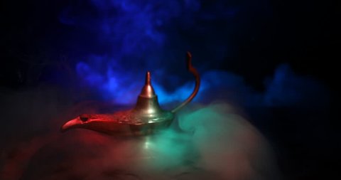 Slider shot.  Antique artisanal Aladdin Arabian nights genie style oil lamp with soft light white smoke. dark smoky toned background. Lamp of wishes