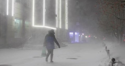 A woman is going through the blizzard in the street in a winter windy night