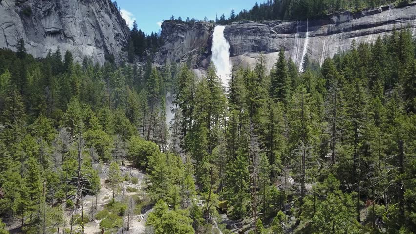 Drone flying over a green forest towards a big waterfall next to rocks on a sunny day the nevada falls in Yosemite National Park California Usa Aerial Drone footage 4K