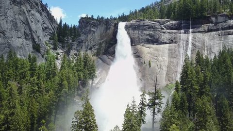 Drone flying over a green forest towards a big waterfall next to rocks on a sunny day the nevada falls in Yosemite National Park California Usa Aerial Drone footage 4K