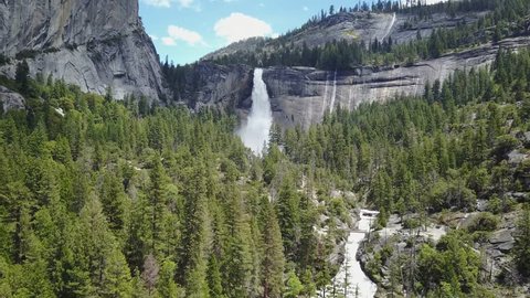 Drone flying over a green forest and a wild river towards a big waterfall next to rocks on a sunny day the nevada falls in Yosemite National Park California Usa Aerial Drone footage 4K