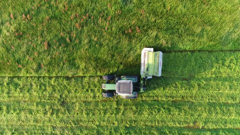 Aerial top down view of tractor cutting grass moving from right to left beautiful fresh green field meadow pasture the cut grass will be dried and become hay and then used as animal silage 4k quality