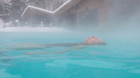 Pretty lady enjoying hot spa in open pool at winter snowy day. Young women bathing the hot steam spa relaxing in open pool at  Winter day 