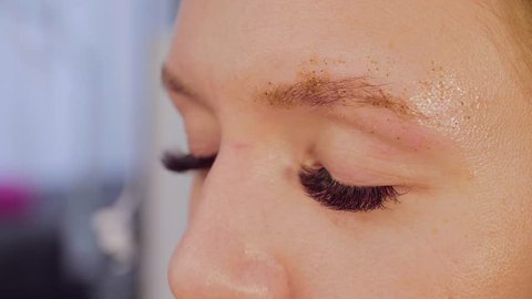 Close up portrait of the woman got eyebrows correction in the beauty salon. Master combing her eyebrow with special brush