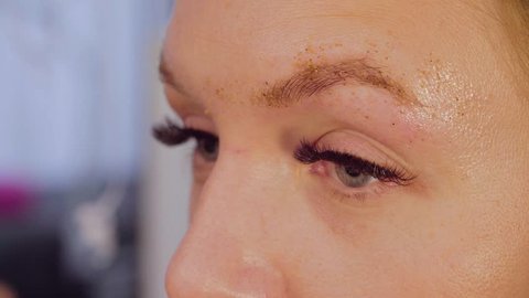 Close up portrait of the woman got eyebrows correction in the beauty salon. Master applying scrab on her eyebrow