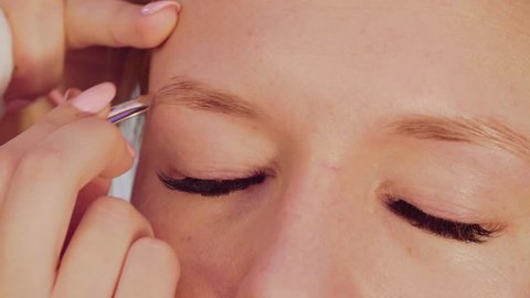 Extreme close up portrait of the woman got eyebrows correction in the beauty salon. Master removing excess hairs.