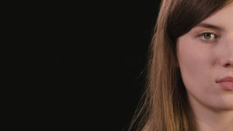 A beautiful young lady's half face smiling against a black background. Close-up shot