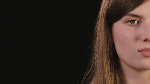 A beautiful young lady's half face smiling against a black background. Close-up shot