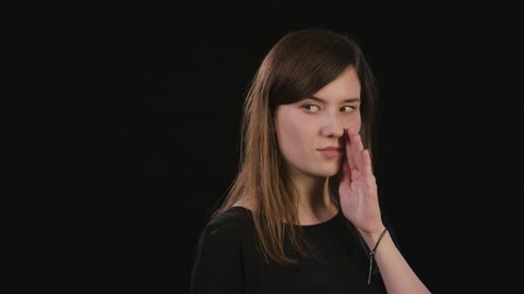 A beautiful young lady showing a whisper gesture against a black background. Medium Shot
