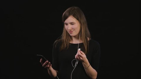 A beautiful young lady listening to music on the phone against a black background. Medium Shot