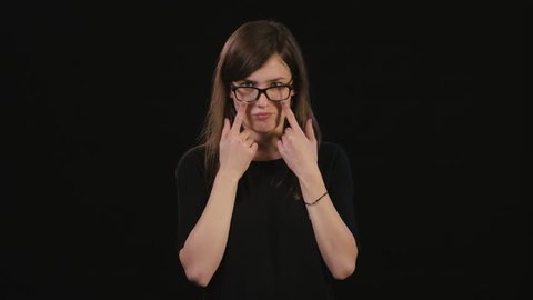 A beautiful young lady takes off her black glasses in confusion against a black background. Medium Shot