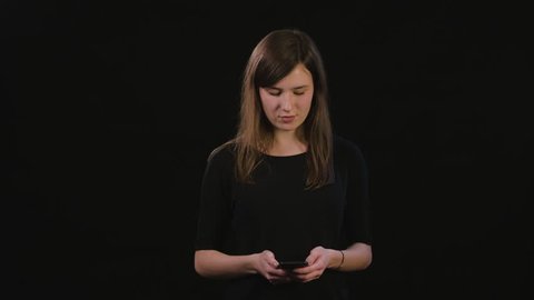 A beautiful young lady using a phone against a black background. Medium Shot