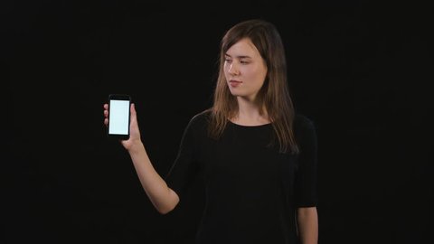 A beautiful young lady pointing her finger at a phone with a white screen against a black background. Medium Shot