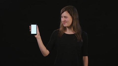 A beautiful young lady pointing her finger at a phone with a white screen against a black background. Medium Shot