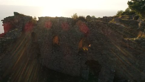 Aerial copter flight during sunset. Close-up view of the ruined Syedra Catsle on the rocky green Taurus Mountains surrounded by Mediterranean sea. Antalya Province in Turkey.
