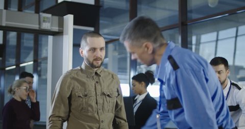 Man in guard uniform conducting checking control with metal detector working with passenger in airport. 4K shot on Red cinema camera.
