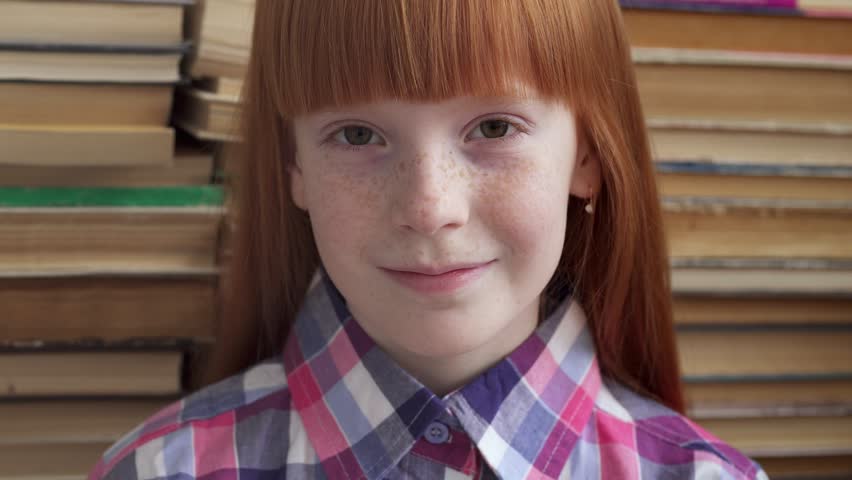 Close-up face of a little happy schoolgirl with freckles on the background of books