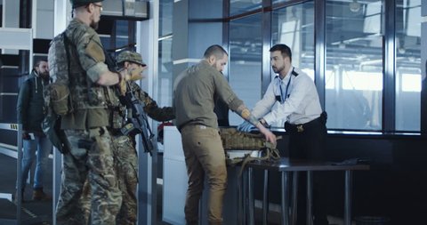 Airport security apprehending a suspect or passenger with men in military uniform pointing a weapon at a kneeling man with his hands on his head at the check-in gate for departures.
