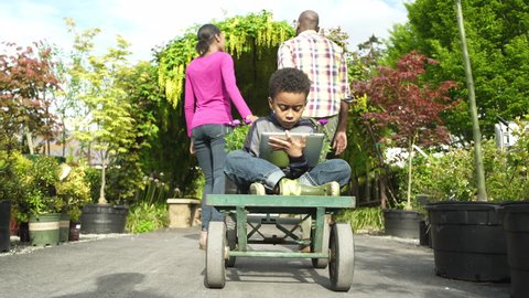 Father and mother pulling their son on a cart in a garden